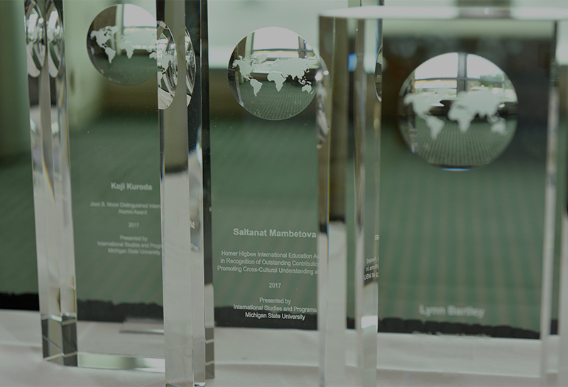 Rectangular glass awards with globes etched into them sit on a table in front of a bright window.