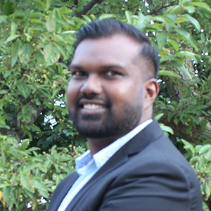 Krishal Prasad smiling in front of leafy backdrop