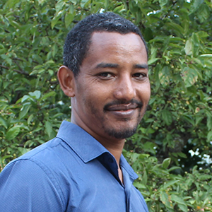 Alemayehu Lamore smiling in front of leafy backdrop