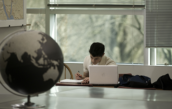 A male student working on a laptop, with a globe in the foreground