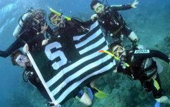 a group of five students diving underwater, displaying a Spartan flag